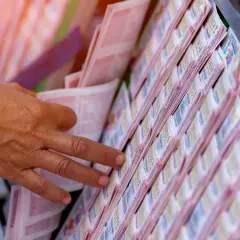 Dłoń wybiera losy loterii. To pokazuje, dlaczego zwycięzcy loterii kredytowych często wpadają w jeszcze większe długi, szukając kolejnej wygranej.