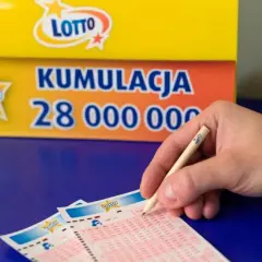 Ręka z ołówkiem Lotto nad kuponami. Tło: baner "Kumulacja 28 000 000". Czy wygrana w małej miejscowości sprawia, że sąsiedzi stają się wrogami?