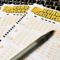 Kupony Eurojackpot leżące na klawiaturze, z długopisem wskazującym na liczby.
