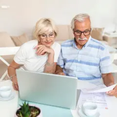 Para seniorów analizuje dokumenty przy laptopie, zastanawiając się, czy emeryci częściej wygrywają w loteriach pożyczkowych skierowanych do seniorów.