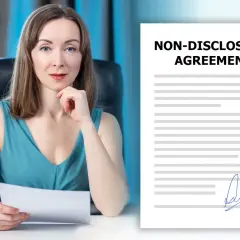 Kobieta z dokumentem w ręku obok umowy o poufności. Czy uczestnicy muszą podpisywać klauzulę poufności dotyczącą wyników przed emisją?