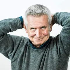 Uśmiechnięty mężczyzna z siwymi włosami, który trzyma ręce za głową. To on jest tym, kto pisze teksty żartów i anegdot, które opowiada prowadzący show.