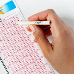Dłoń z ołówkiem zaznacza liczby na kuponie gry Lotto.