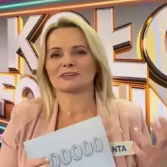 Kobieta w różowym żakiecie trzyma kartkę z napisem "00000" na tle logo "Koło Fortuny".