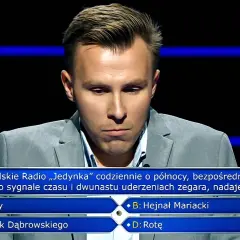 Młody mężczyzna w szarym garniturze zastanawia się nad pytaniem z teleturnieju. Jakie pytania zadaje psycholog zwycięzcom lotto w poradniku milionera?
