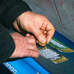 Dłonie zdrapują zdrapki lotto. Poznaj prawdziwe powody dla których zwycięzcy loterii ukrywają swoją tożsamość, by uniknąć kłopotów.