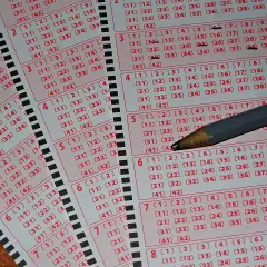 Kaskada kuponów lotto z zaznaczonymi liczbami i ołówkiem. Tabela wygranych czeka na szczęśliwców.