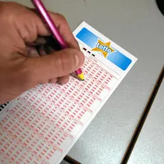 Dłoń z różowym ołówkiem zaznacza liczby na kuponie Lotto.