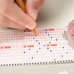 Ręka zaznacza liczby na kuponie lotto, zastanawiając się, ile do wygrania w mini lotto.