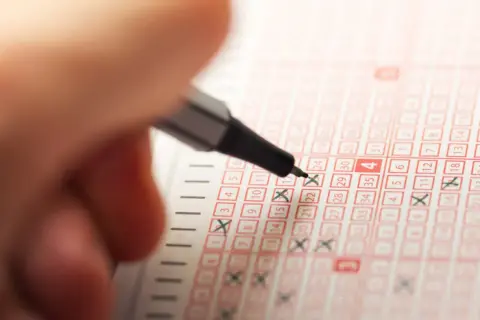Ręka zaznacza liczby na kuponie lotto. Odkryj sekrety produkcji losowań lotto na żywo, czego nie widzą widzowie.