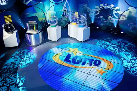 Scena studia lotto z kulami losującymi i ekranem z logo. Czy lottomilionerzy dostają ochronę osobistą od organizatora loterii?
