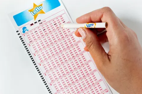 Dłoń z ołówkiem zaznacza liczby na kuponie Lotto. Czy system lotto online jest bezpieczniejszy od papierowych kuponów?