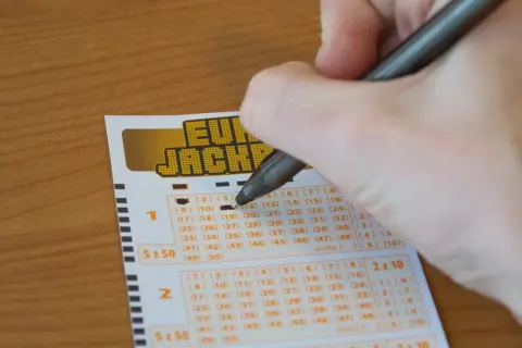 Ręka zaznacza liczby na kuponie Eurojackpot. Czy wygrana w Eurojackpot w Polsce jest opodatkowana inaczej niż w Lotto?