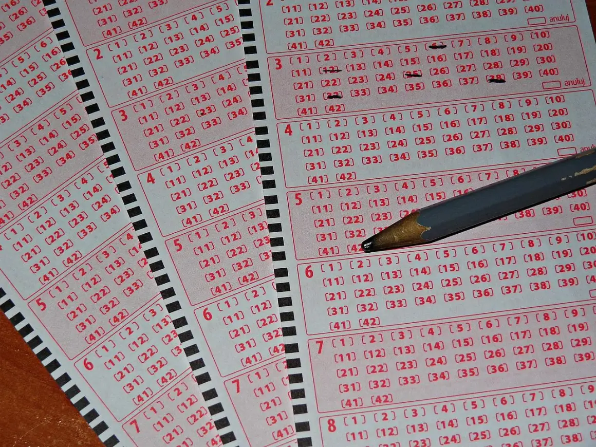 Kaskada kuponów lotto z zaznaczonymi liczbami i ołówkiem. Tabela wygranych czeka na szczęśliwców.