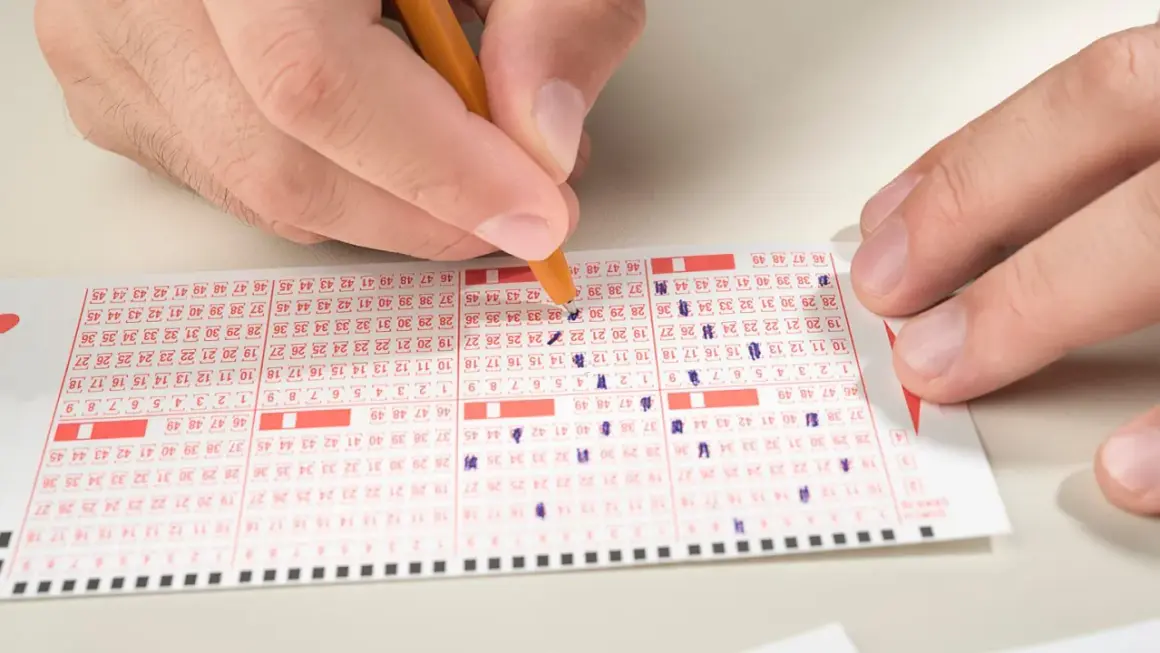 Ręka zaznacza liczby na kuponie lotto, zastanawiając się, ile do wygrania w mini lotto.