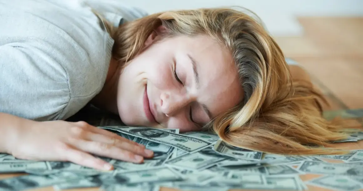 Uśmiechnięta kobieta śpi na stosie banknotów dolarowych. Marzy o tym, czy polskie gwiazdy rzeczywiście biorą udział w międzynarodowych kumulacjach.
