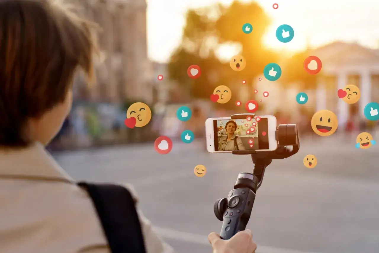 Czy influencerzy promujący szybkie pożyczki z nagrodami sami z nich korzystają? Kobieta nagrywa siebie na telefonie, a wokół latają emotikony.