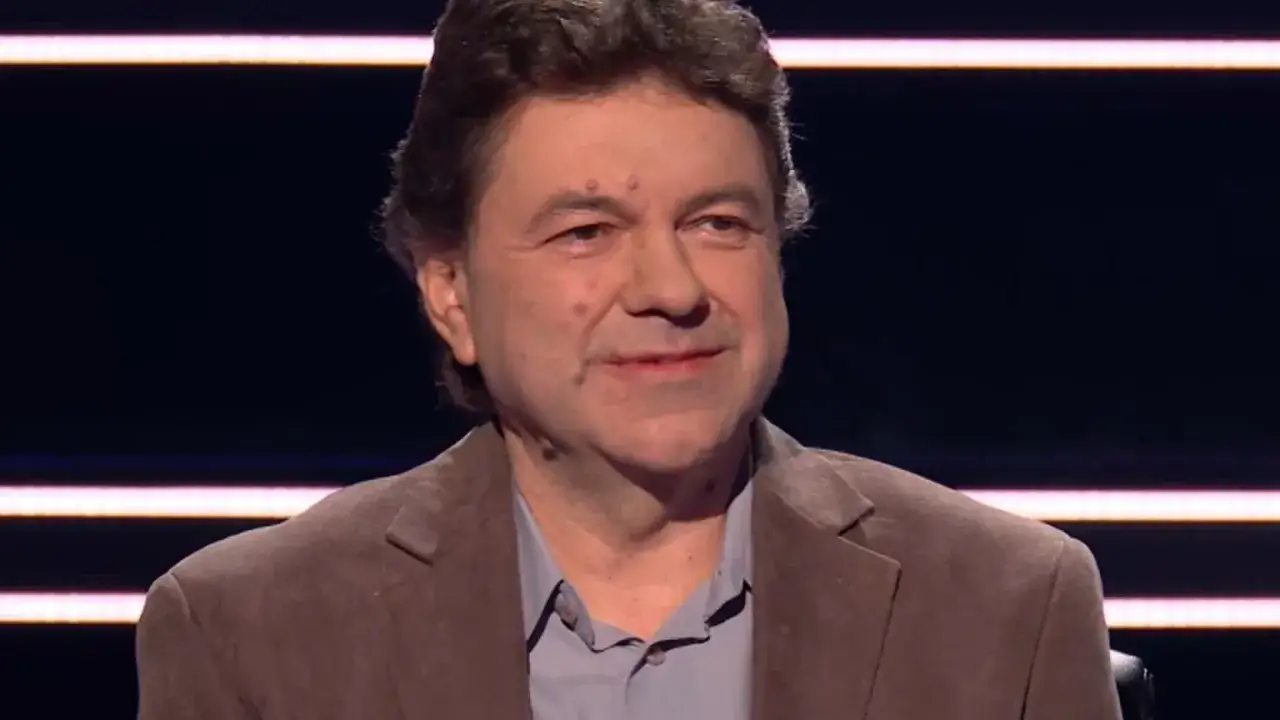 Mężczyzna w brązowej marynarce, zastanawia się, czy nagrody rzeczowe w programie są sponsorowane czy kupowane przez stację.