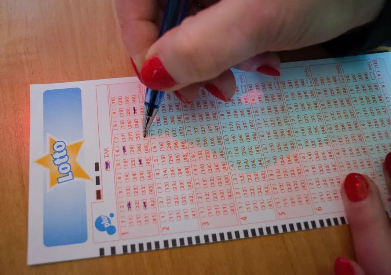Ręka z czerwonymi paznokciami zaznacza liczby na kuponie Lotto. Pamiętaj, dlaczego po wygranej w Eurojackpot nie wolno od razu rzucać pracy.