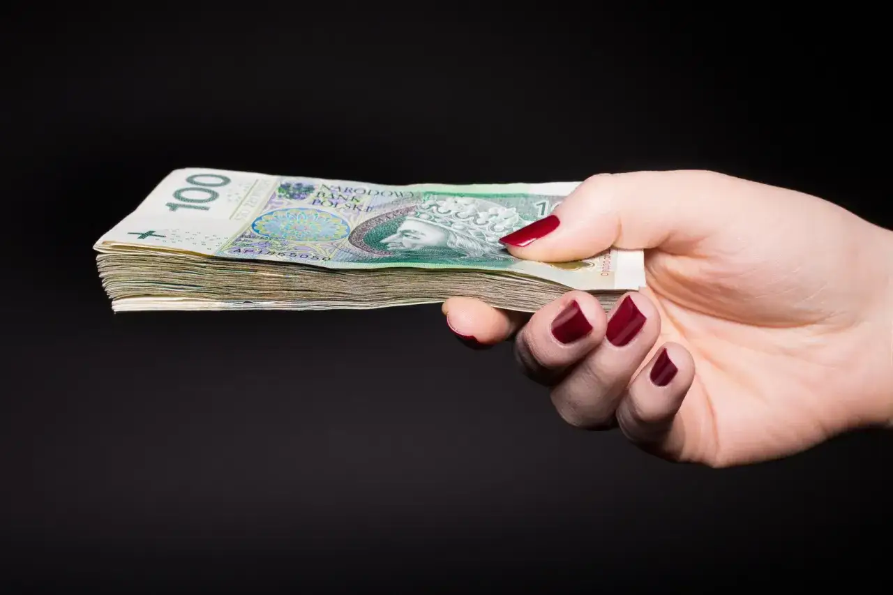 Dłoń z pomalowanymi paznokciami trzyma stos banknotów 100 zł. Czy można wymienić nagrodę rzeczową z loterii kredytowej na gotówkę?