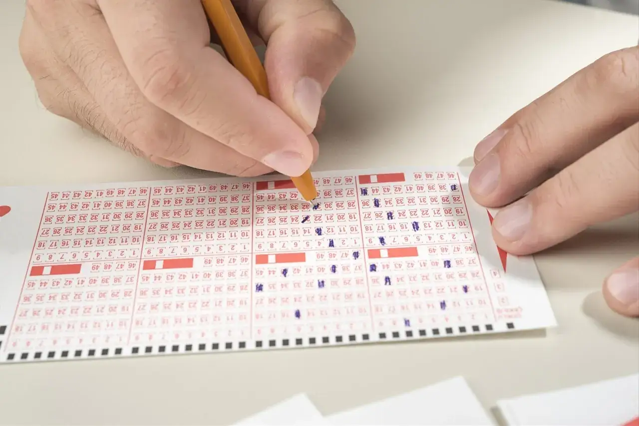 Ręka z ołówkiem zaznacza liczby na kuponie Lotto. Czy to właśnie tutaj kryje się odpowiedź, dlaczego 17 milionów złotych z lotto przepadło i nikt ich nie odebrał?