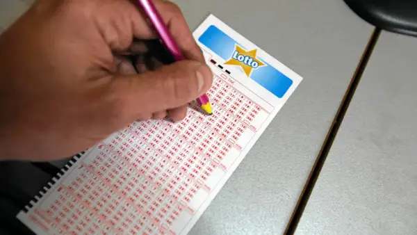 Ręka z ołówkiem zaznacza liczby na kuponie Lotto. Czy wartość głównej wygranej w lotto jest znana przed losowaniem?