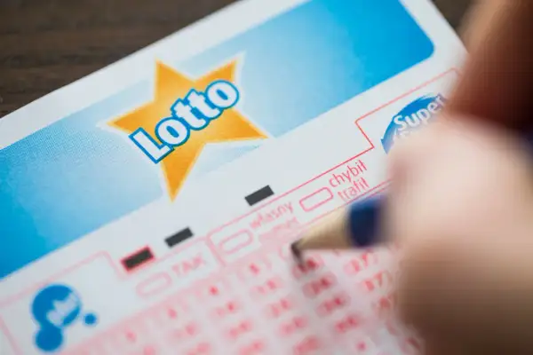 Dłoń z ołówkiem zaznacza liczby na kuponie Lotto. Czy to te same, dlaczego ludzie skreślają te same liczby co 80 innych zwycięzców?