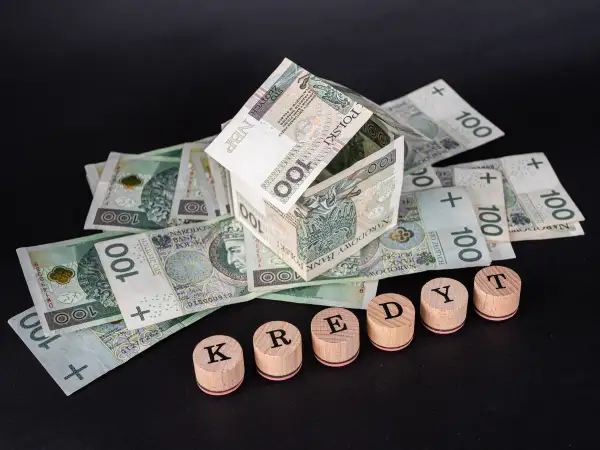 Dom z banknotów 100 zł i drewniane klocki z napisem "KREDYT". Uważaj na najczęstsze błędy w umowach pożyczkowych, które wykluczają z udziału w losowaniu.