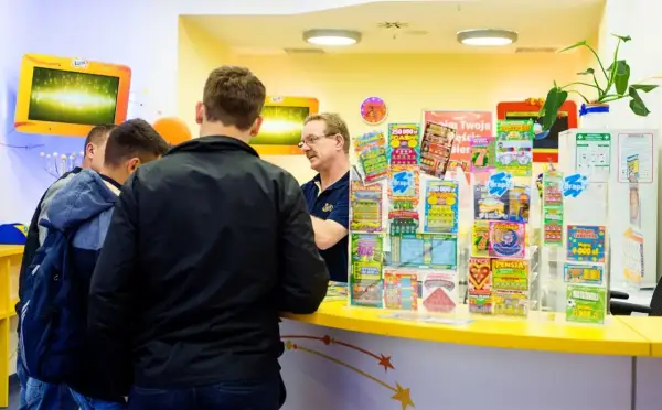 Mężczyźni stoją przy ladzie, na której widać wiele zdrapek Lotto. Czy na Orlenie są zdrapki Lotto? Tak, jak widać na zdjęciu.